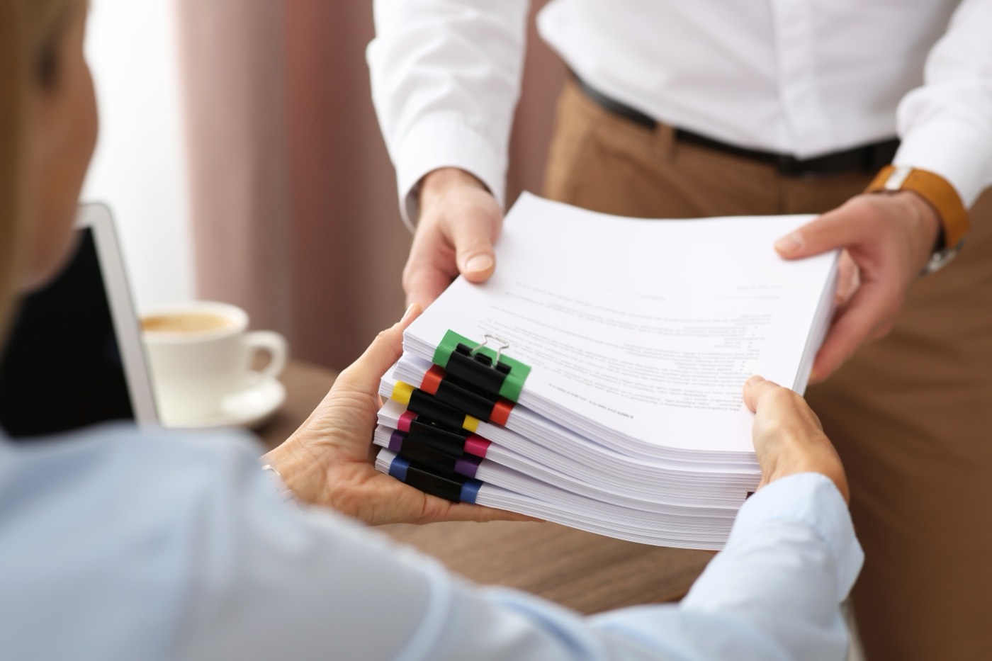A thick tabbed payroll file being handed from one colleague to another
